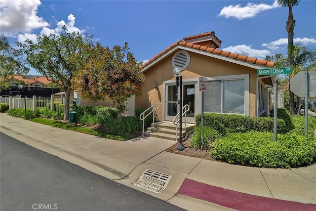 view of front of house with stucco siding, a tiled roof, and fence