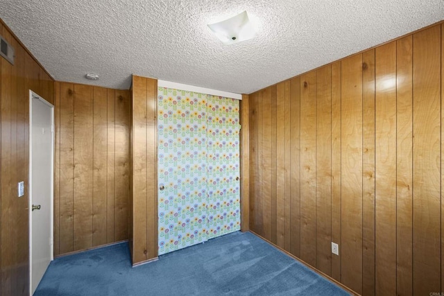 carpeted spare room featuring wooden walls and a textured ceiling