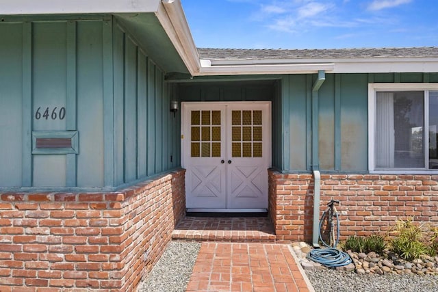 entrance to property featuring brick siding, a shingled roof, and board and batten siding