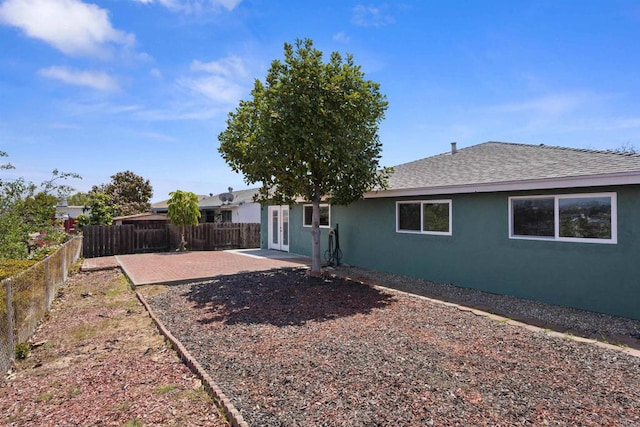 rear view of property with roof with shingles, stucco siding, a fenced backyard, french doors, and a patio