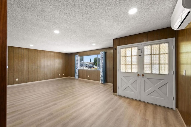 interior space with a textured ceiling, a wall mounted AC, baseboards, wooden walls, and light wood-style floors