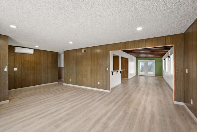 unfurnished living room featuring wooden walls, a wall unit AC, and light wood-style flooring
