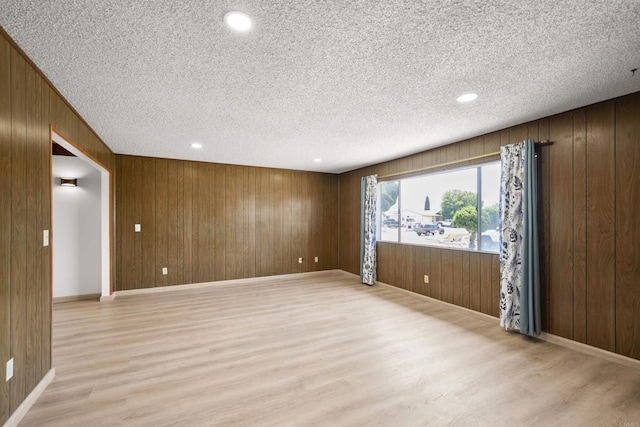 unfurnished room featuring recessed lighting, a textured ceiling, wood walls, and light wood-style flooring