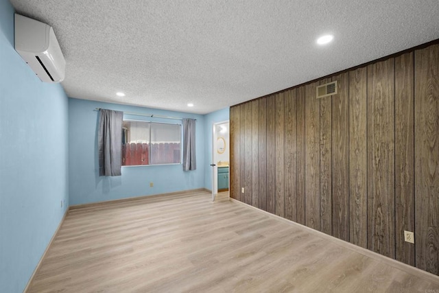 spare room with wooden walls, a wall mounted air conditioner, a textured ceiling, wood finished floors, and visible vents