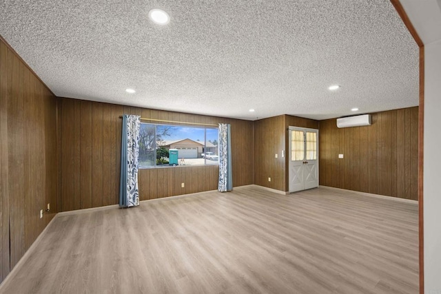 empty room featuring an AC wall unit, wood walls, and light wood-style flooring