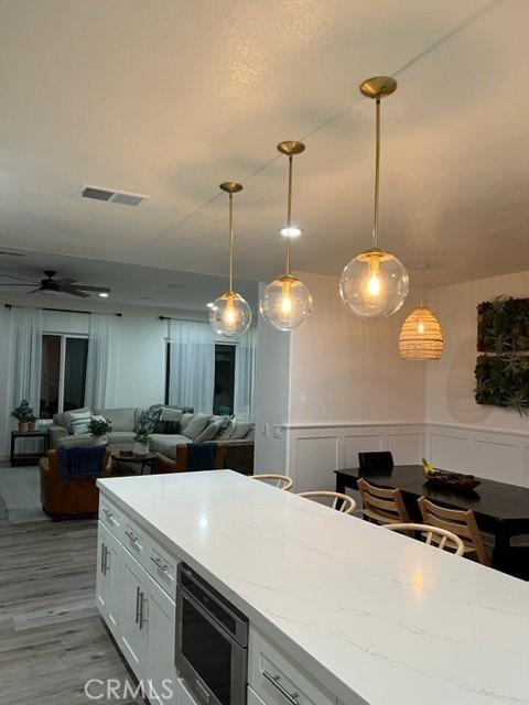 27041 S Ridge Dr, Mission Viejo, CA 92692 - kitchen with stainless steel microwave, open floor plan, pendant lighting, white cabinetry, and wainscoting
