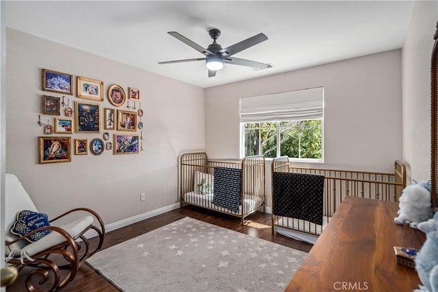 bedroom featuring a nursery area, a ceiling fan, baseboards, visible vents, and dark wood-style floors