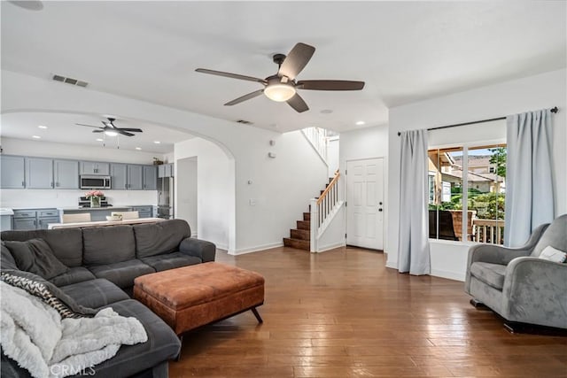 living room with visible vents, wood-type flooring, stairway, arched walkways, and a ceiling fan