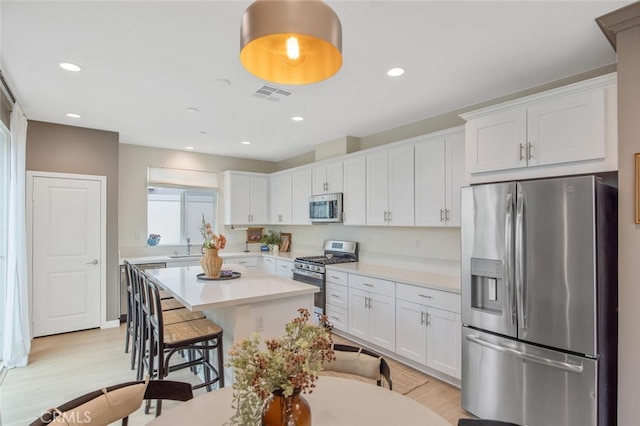 18147 Jupiter Ln, Saugus, CA 91350 - kitchen featuring appliances with stainless steel finishes, a breakfast bar area, light wood-type flooring, white cabinets, and light countertops