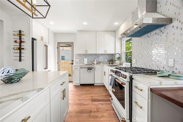 kitchen with tasteful backsplash, light stone countertops, a sink, white appliances, and wall chimney exhaust hood