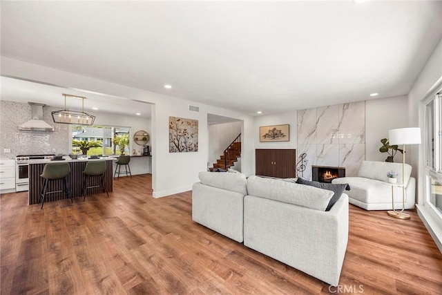 living area featuring stairs, recessed lighting, wood finished floors, a high end fireplace, and visible vents