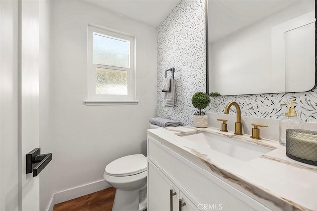 half bathroom with toilet, baseboards, wood finished floors, and vanity