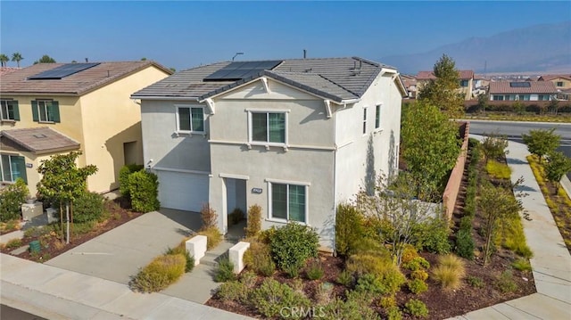 traditional home featuring stucco siding, roof mounted solar panels, concrete driveway, an attached garage, and a residential view