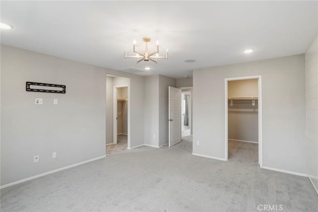 unfurnished bedroom featuring light carpet, a walk in closet, a chandelier, baseboards, and a closet