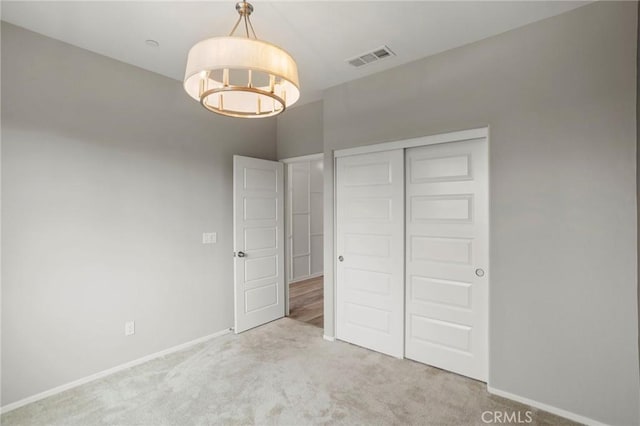 unfurnished bedroom featuring visible vents, carpet floors, baseboards, a closet, and a chandelier