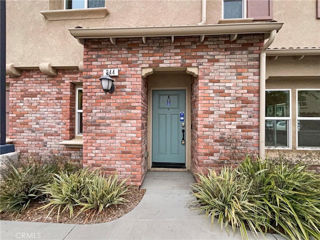 view of exterior entry with stucco siding and brick siding