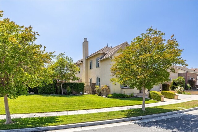 view of side of home with a chimney, a lawn, stucco siding, and a tiled roof