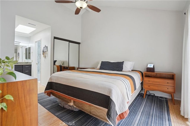 bedroom featuring a ceiling fan, ensuite bathroom, vaulted ceiling, light wood-type flooring, and visible vents