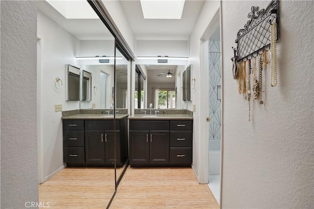 full bath with a skylight, a textured wall, a sink, and wood finished floors