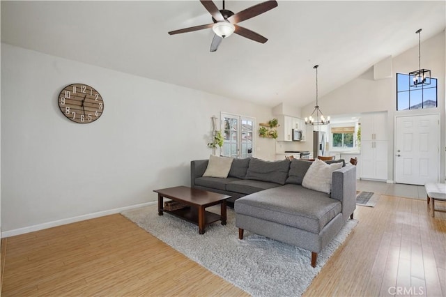 living room with baseboards, light wood-style flooring, ceiling fan with notable chandelier, and high vaulted ceiling