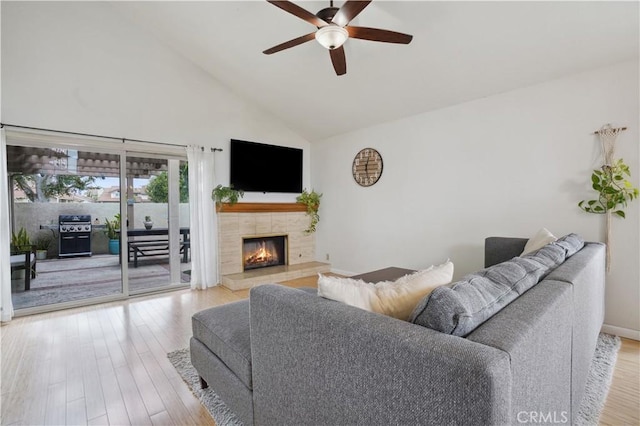 living room with light wood-style flooring, ceiling fan, high vaulted ceiling, and a tile fireplace