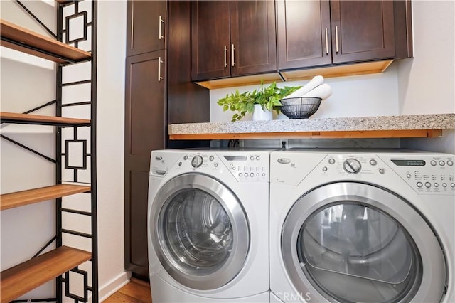 clothes washing area with cabinet space, washing machine and clothes dryer, wood finished floors, and baseboards