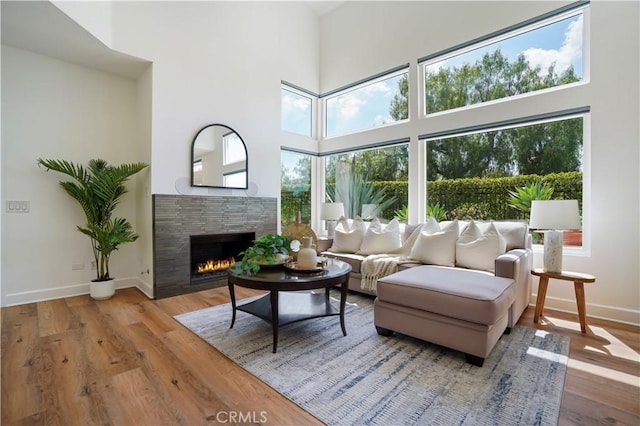living room featuring wood finished floors, a high ceiling, baseboards, and a tile fireplace