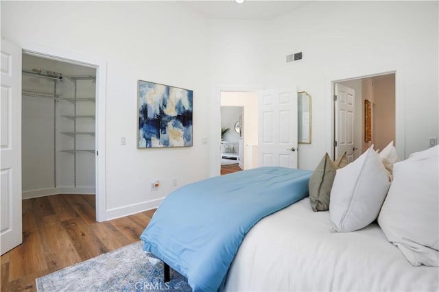 bedroom featuring a walk in closet, a closet, baseboards, visible vents, and wood finished floors