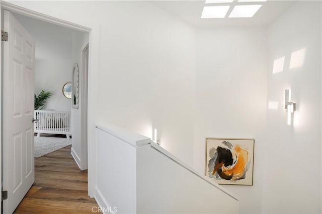 corridor featuring a skylight, an upstairs landing, and wood finished floors