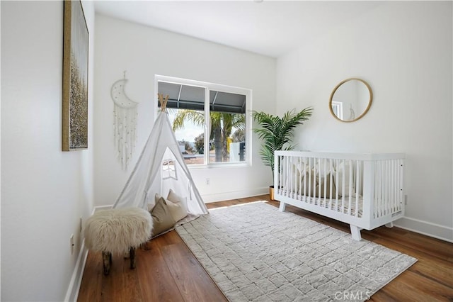 bedroom featuring a crib, wood finished floors, and baseboards