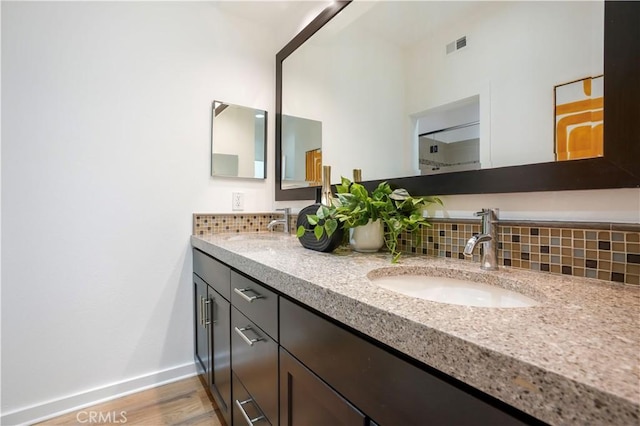 bathroom with a sink, decorative backsplash, baseboards, and wood finished floors