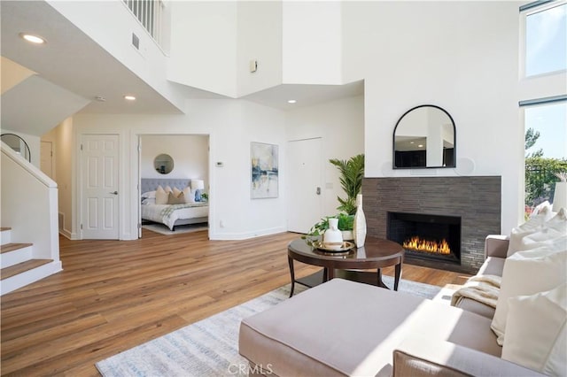 living area featuring a towering ceiling, a fireplace, stairway, light wood-style flooring, and baseboards