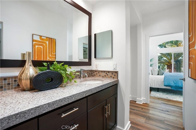 ensuite bathroom with ensuite bath, decorative backsplash, wood finished floors, and vanity