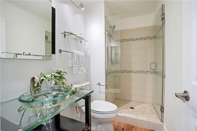 full bath with a stall shower, toilet, a sink, and wood finished floors