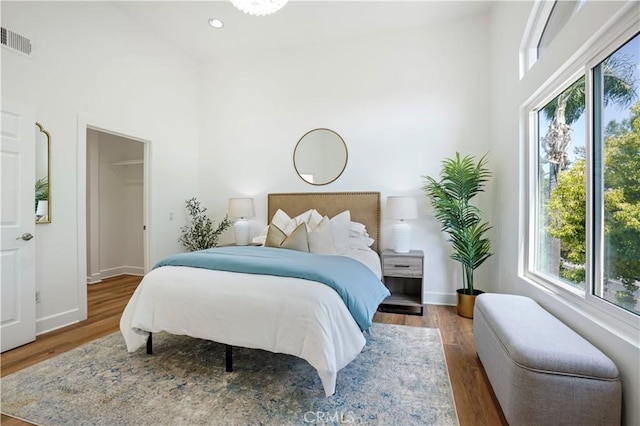 bedroom with wood finished floors, a high ceiling, visible vents, baseboards, and recessed lighting