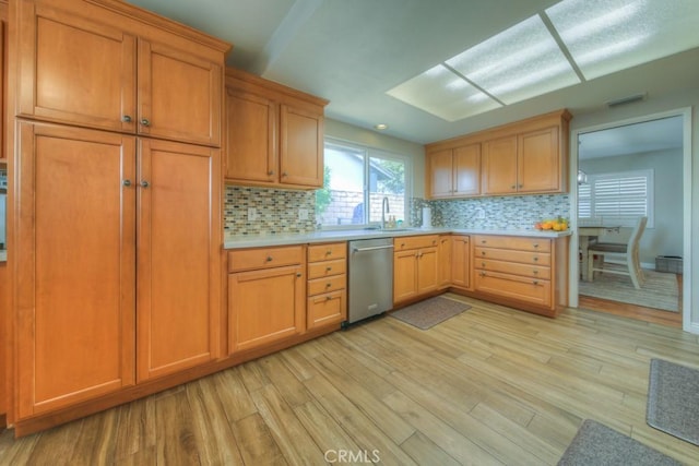 kitchen featuring stainless steel dishwasher, a sink, backsplash, light wood-style floors, and light countertops