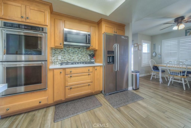 kitchen featuring a ceiling fan, stainless steel appliances, backsplash, light countertops, and light wood-style floors