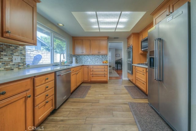 kitchen with light wood finished floors, stainless steel appliances, tasteful backsplash, and a sink