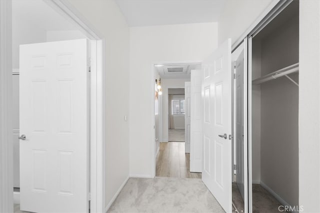 hall with baseboards, visible vents, and light carpet