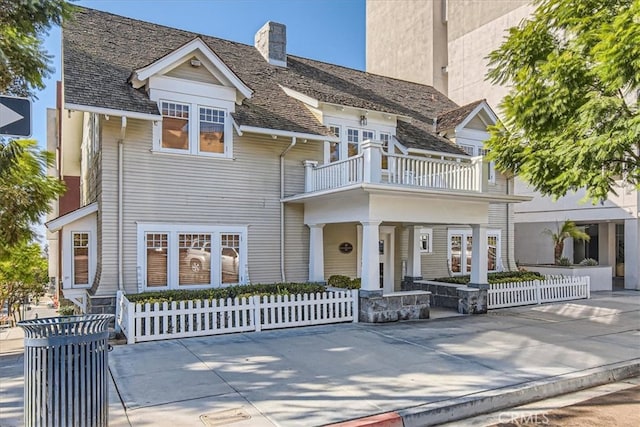 view of front facade featuring a porch, a fenced front yard, a balcony, and a chimney