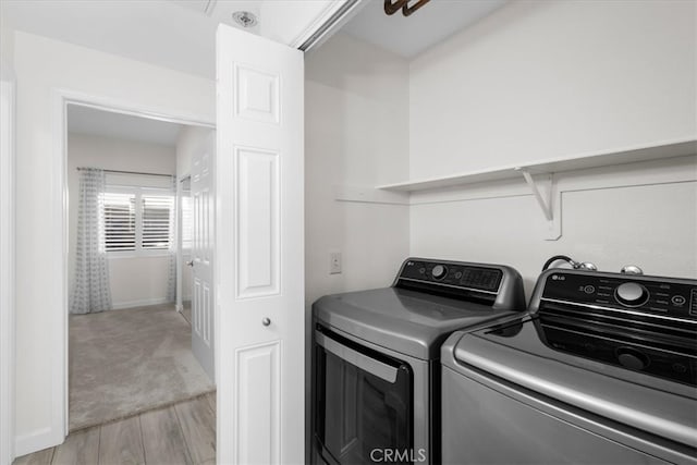 washroom with laundry area, light wood finished floors, washer and dryer, and light colored carpet