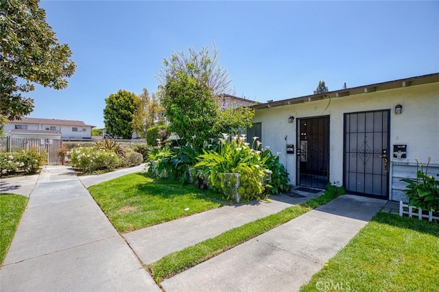 view of front of home with fence, a front lawn, and stucco siding