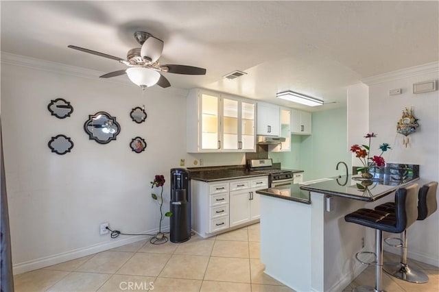 kitchen with visible vents, dark countertops, a breakfast bar area, under cabinet range hood, and stainless steel range with gas stovetop