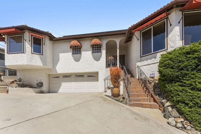 mediterranean / spanish-style home with stairs, stucco siding, an attached garage, and driveway
