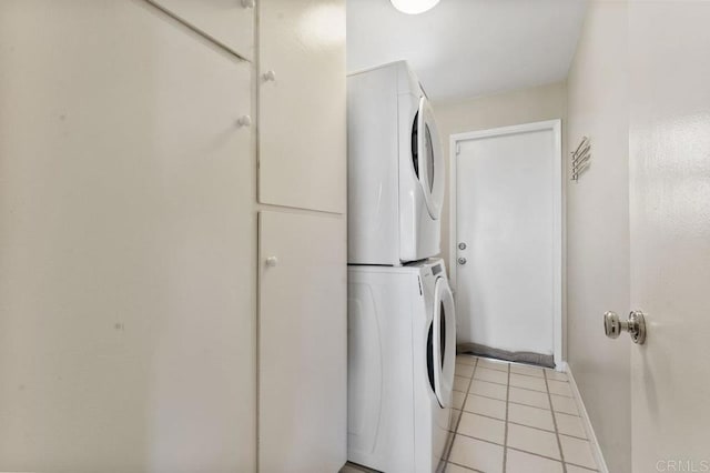 laundry area with baseboards, laundry area, stacked washer and dryer, and light tile patterned flooring