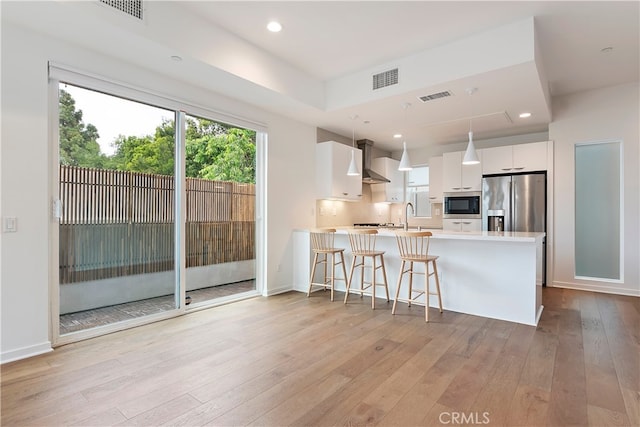 kitchen with visible vents, wall chimney range hood, light countertops, built in microwave, and white cabinets