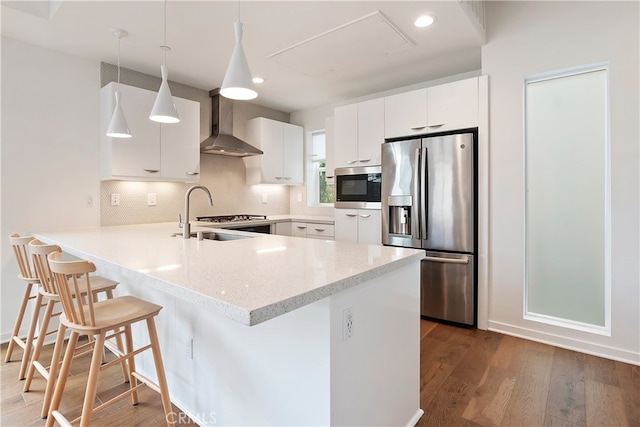 kitchen with backsplash, a sink, a peninsula, stainless steel appliances, and wall chimney exhaust hood