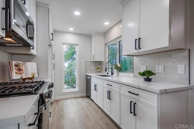kitchen featuring light stone countertops, a sink, stainless steel appliances, decorative backsplash, and light wood-type flooring