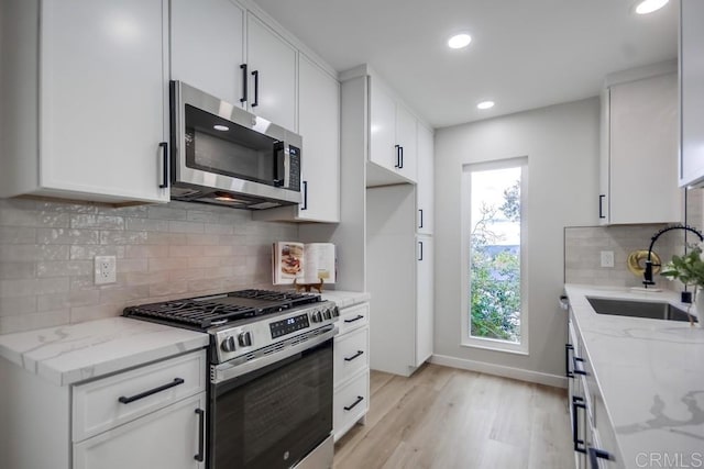 kitchen featuring light stone counters, a sink, light wood finished floors, and appliances with stainless steel finishes