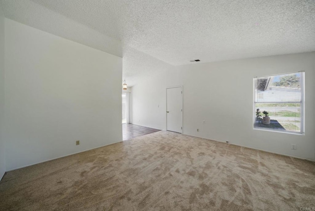 spare room featuring carpet floors, a textured ceiling, vaulted ceiling, and visible vents